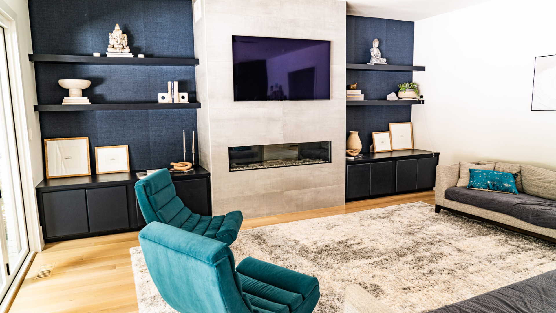 Living room with navy built-in cabinetry, a stone fireplace, mounted television and teal swivel chairs